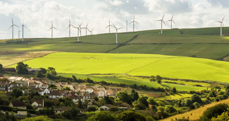 A number of wind turbines on a green grass hill